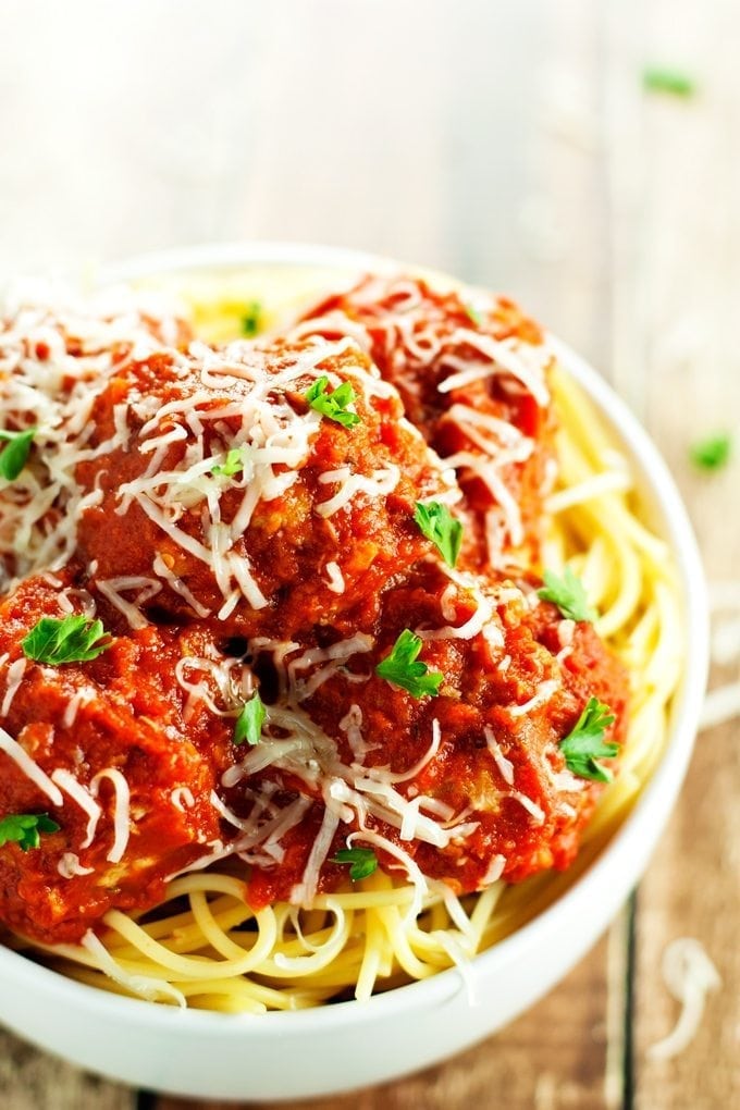 A closeup of a bowl full of baked turkey meatballs smothered in tomato sauce and topped with parmesan cheese.