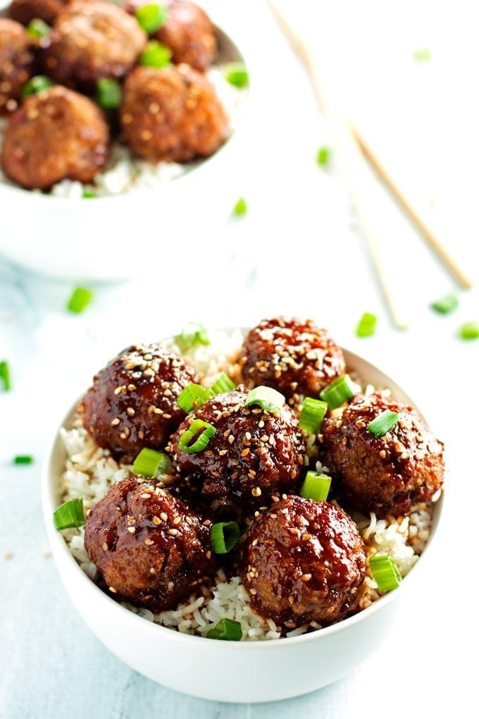 Two bowls overflowing with beef teriyaki meatballs. Served over rice and topped with sesame seeds and green onions.