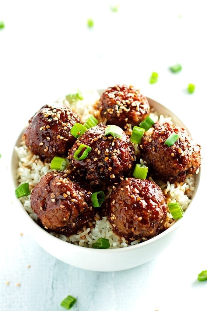 a bowl full of beef teriyaki meatballs served over rice and topped with green onions and sesame seeds.