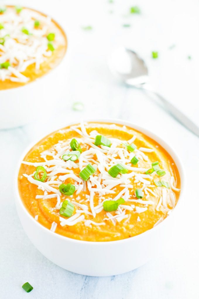 two creamy bowls of cauliflower sweet potato soup topped with green onions and shredded cheese