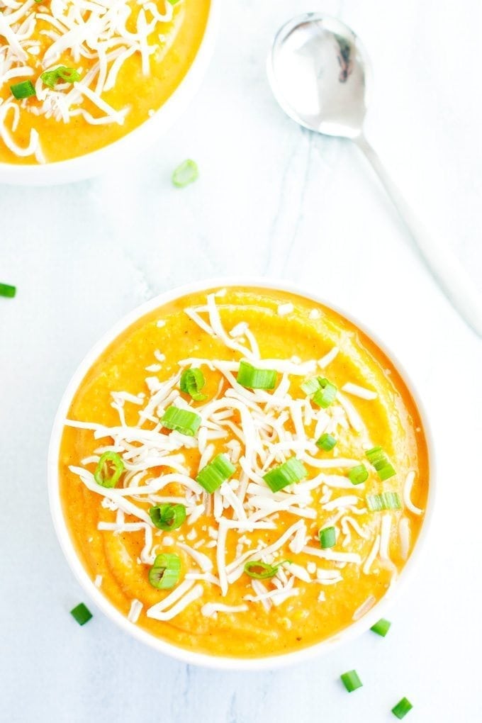 two bowls of cauliflower sweet potato soup served with a spoon