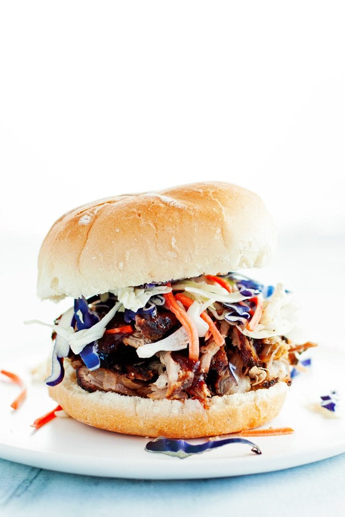 pulled pork sandwich dripping with bbq sauce on a toasted bun topped with colorful purple cabbage and shredded carrots