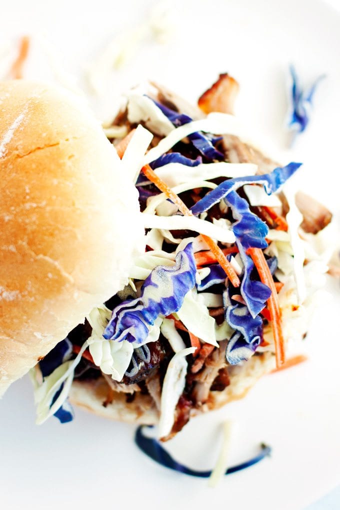 top view of pulled pork sandwich topped with colorful purple cabbage and shredded carrots