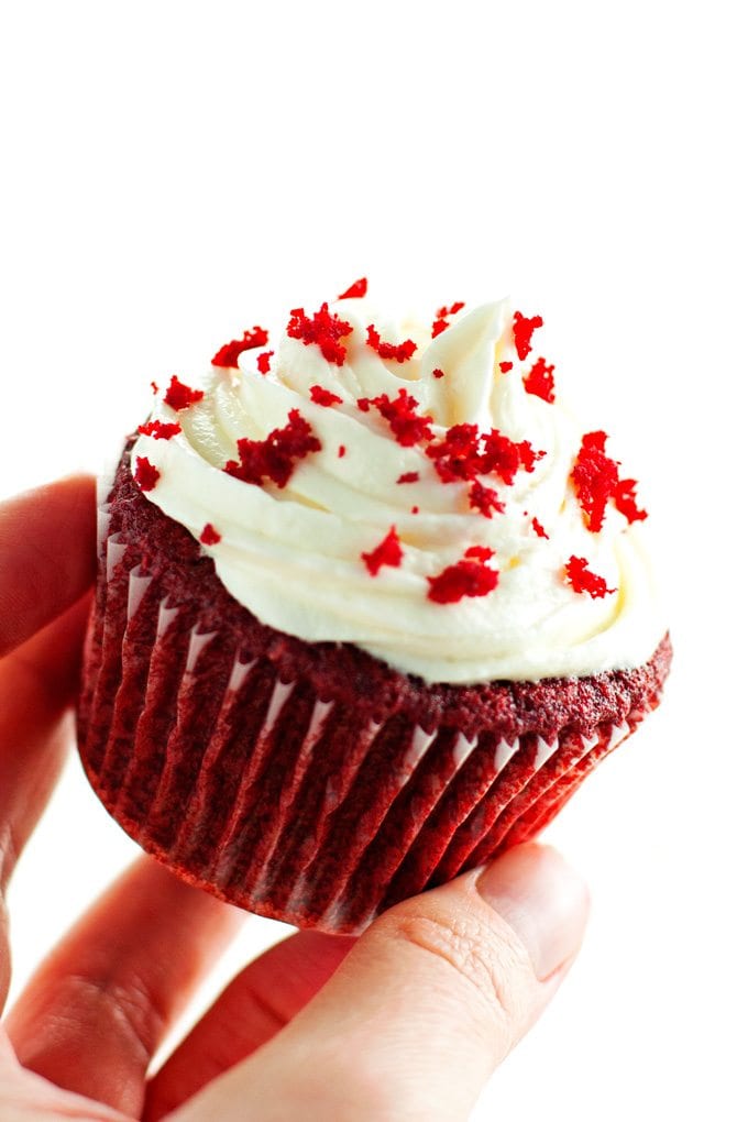 red velvet cupcake being held at a slant to display piped cream cheese frosting