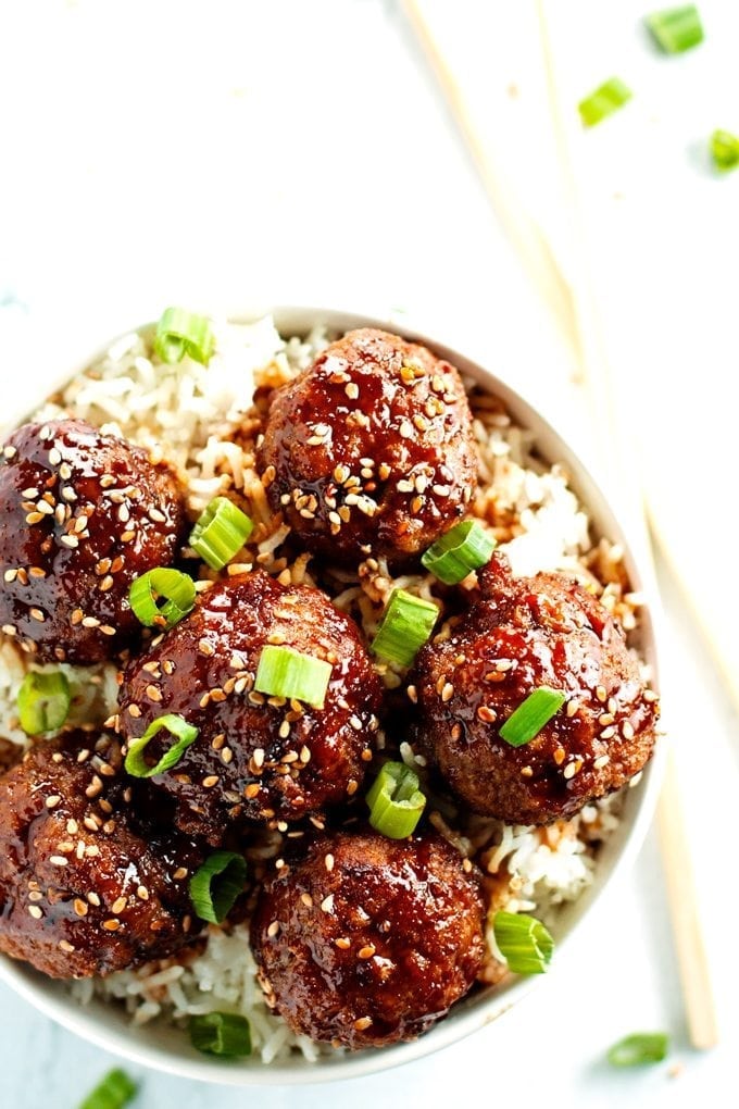 close up over head shot of beef teriyaki meatballs served over rice and topped with green onions and sesame seeds.